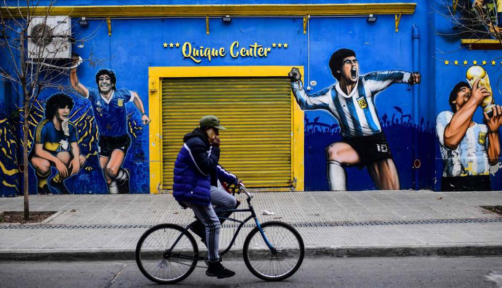 Un hombre monta su bicicleta frente a una tienda deportiva cerrada en el barrio de La Boca en Buenos Aires (Argentina). (AFP / Ronaldo SCHEMIDT).